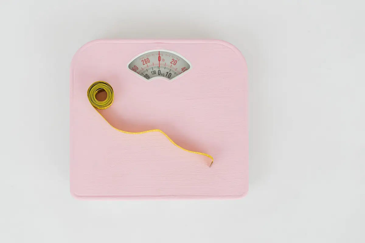 Pèse-personne rose et mètre ruban jaune vus de dessus, pour le calcul de l'IMC
